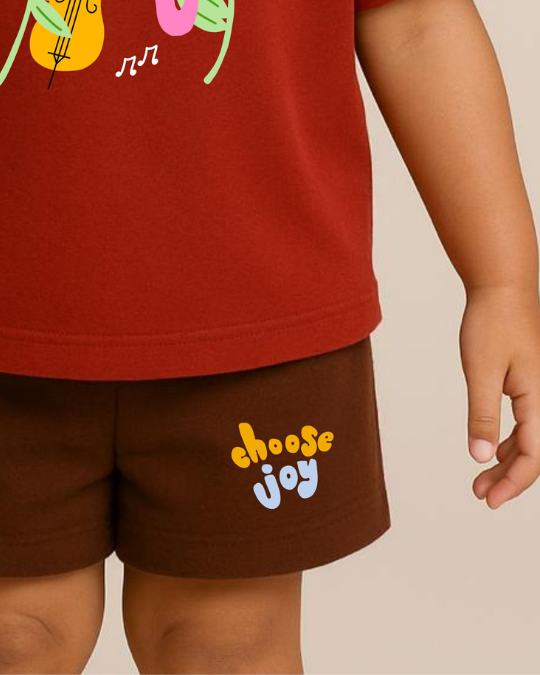 Child wearing a red shirt with colorful graphics and brown shorts with 'choose joy' text.