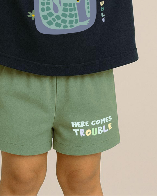 Green shorts with 'Here Comes Trouble' text worn by a child, against a neutral background