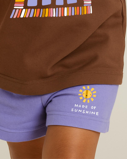 Brown top with colorful design and purple shorts with 'Made of Sunshine' text on a beige background
