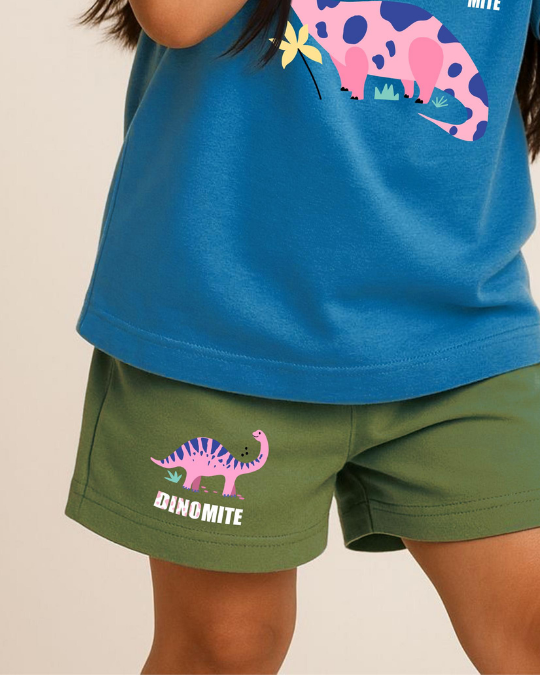 Child wearing a blue shirt with dinosaur design and green shorts with 'DINOMITE' text on a beige background