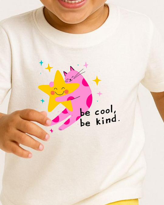 Child wearing a white shirt with a colorful graphic and 'be cool, be kind' text.
