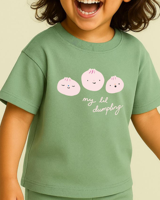 Child wearing a green t-shirt with pink dumpling graphics and text on a beige background