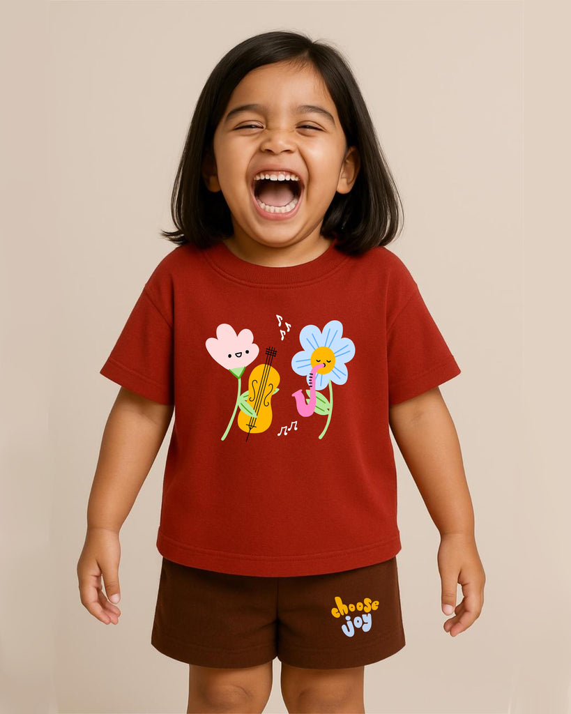 Child wearing a red t-shirt with colorful flower designs and brown shorts on a beige background
