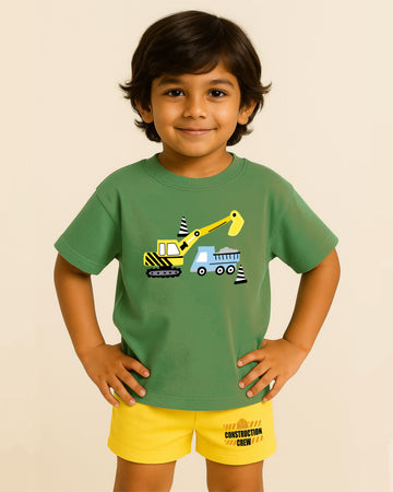 Child wearing a green t-shirt with construction vehicle graphics and yellow shorts on a beige background