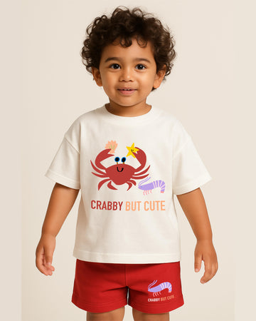 Child wearing a white t-shirt with a red crab graphic and text, standing against a plain background.