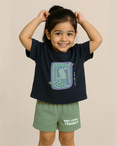 Child wearing a navy blue t-shirt with a graphic design and green shorts on a beige background