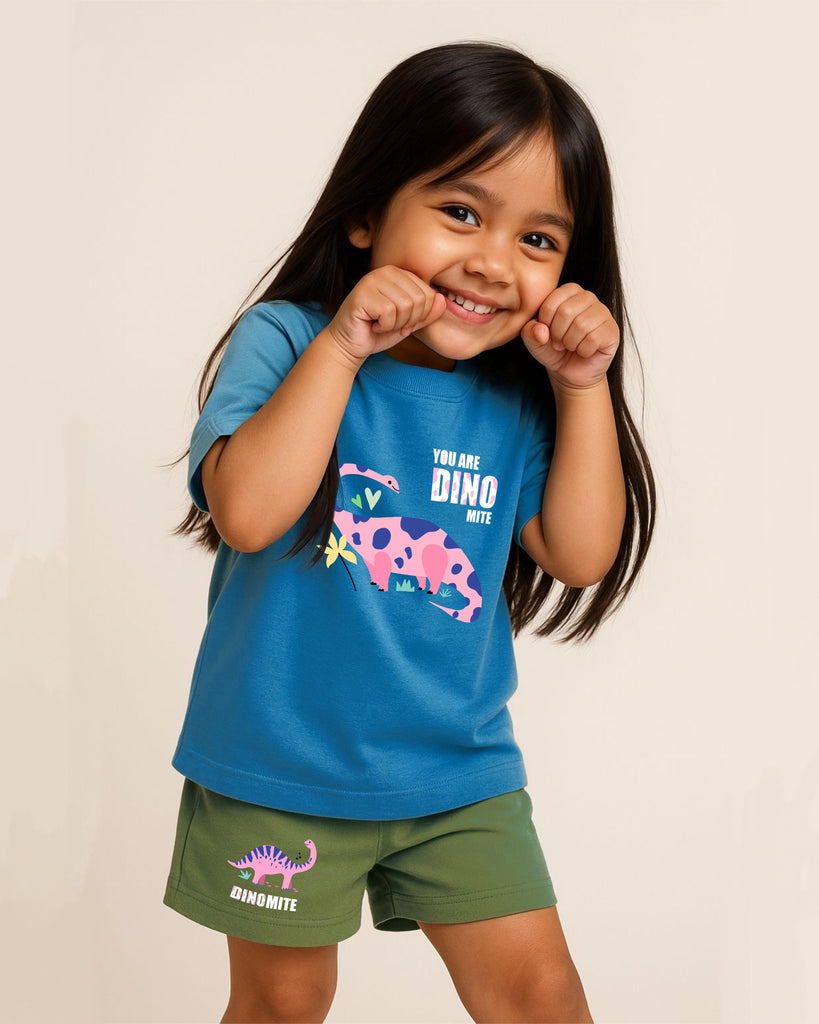 Young girl wearing a blue shirt and green shorts with dinosaur graphics on a beige background